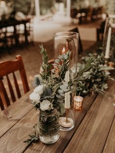 a wooden table topped with vases filled with flowers and greenery next to candles