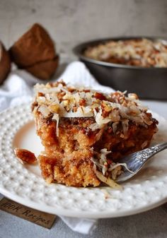 a piece of cake on a white plate with a fork and coconut in the background