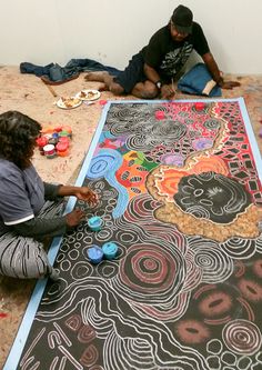 two people are sitting on the floor painting