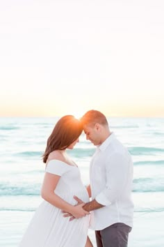 a pregnant couple standing on the beach at sunset