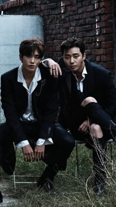 two young men sitting next to each other in front of a brick wall and grass