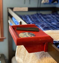 a red tray with a pen on it sitting on top of a wooden bed frame