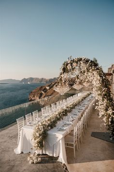 a long table with white flowers and greenery is set up for an outdoor wedding