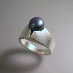 "This is a very contemporary ring done with a beautiful black pearl. The pearl has grey tones with a bluish overcastthe pictures do not do it justice....these pearls have a great \"luster\". The ring is cast, and is done in the lost wax process. It is completely hand finished. Pearl size: 8mm Ring height: 7.5mm Ring width: 12mm This ring is available in either brush finish, or high polish. See above photos of both finishes. Made to order, allow about 2 weeks for delivery." Modern Wedding Pearl Ring, Pearl Ring Design, Black Pearl Jewelry, Contemporary Silver Jewelry, Black Pearl Ring, Chunky Silver Rings, Gold Color Ring, Seashell Jewelry, Egyptian Jewelry