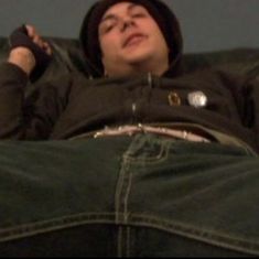 a man laying on top of a couch with his hands in his pockets and wearing a hoodie