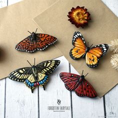 four butterflies sitting on top of a piece of brown paper next to flowers and leaves