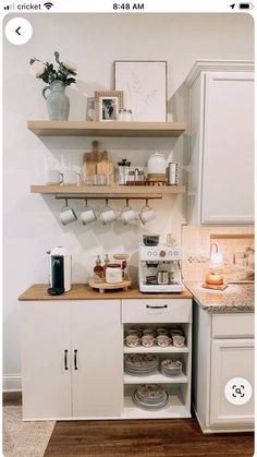 a kitchen with white cabinets and shelves filled with coffee pots, mugs and other items