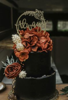 there is a black cake with orange flowers on it and the word always spelled in gold