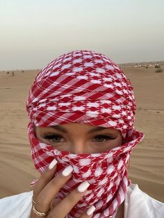 a woman wearing a red and white patterned head scarf covering her face in the desert