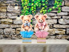 two teddy bears sitting on top of vases in front of a stone wall with ivy