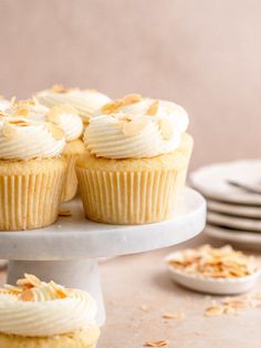 cupcakes with white frosting and toasted almonds on a cake stand