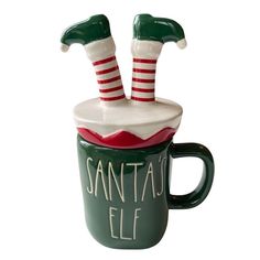 a ceramic mug with two christmas stockings on top and santa's elf legs sticking out of it