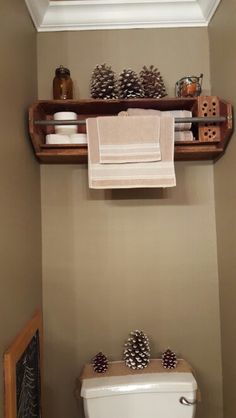 a toilet in a bathroom with pine cones on the shelf and towels hanging above it