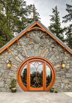 a stone building with an arched wooden door and glass windows on the outside, surrounded by pine trees