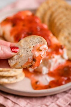 a hand holding a piece of bread over a plate with pizza and crackers on it