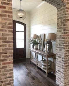 a hallway with brick walls and wooden floors, two lamps on either side of the console table