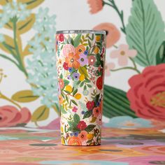 a colorful flowered cup sitting on top of a table next to a floral wallpaper