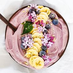 a bowl filled with fruit and flowers on top of a white table cloth next to a wooden spoon