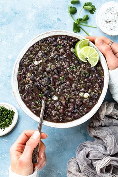 someone holding a spoon in a bowl filled with black beans and cilantros