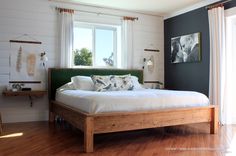 a bed sitting on top of a hard wood floor next to a window with white curtains