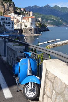 a blue scooter parked on the side of a road next to a body of water