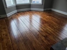 an empty room with hard wood floors and two windows