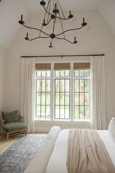 a bed sitting under a window next to a chair and lamp in a room with white walls