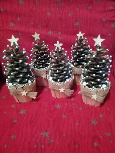 four small pine cones with silver stars and bows on red fabric, all decorated in different sizes