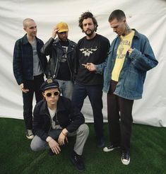 four men are standing in front of a white backdrop and one man is wearing sunglasses