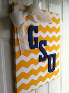 a yellow and white door hanger with the word g s u painted on it