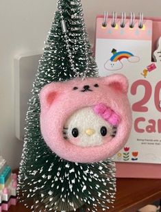 a hello kitty christmas ornament hanging from a tree on a desk next to a calendar