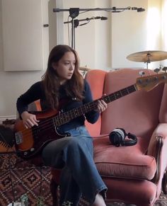 a woman sitting on top of a pink couch holding a guitar