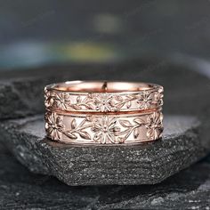 two gold wedding bands with flowers on them sitting on top of a black stone slab