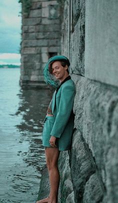 a woman leaning against a stone wall next to the water