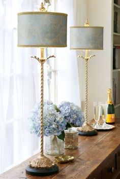 two lamps sitting on top of a wooden table next to a vase filled with flowers