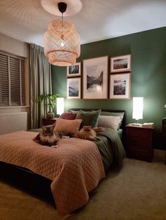 a bedroom with green walls and pictures on the wall, two cats laying on the bed