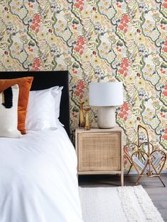 a bed sitting next to a night stand with a lamp on top of it in front of a floral wallpaper