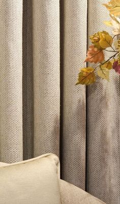 a white chair sitting in front of a window covered in curtains and fall colored leaves