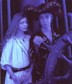 two people standing next to each other in front of a steering wheel on a ship