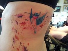 a woman's thigh with watercolor splashes and a hummingbird tattoo on it