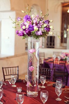 a tall vase filled with purple flowers on top of a table