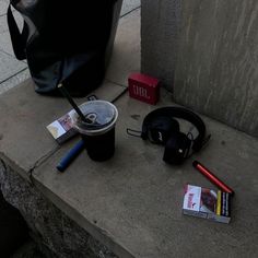 a coffee cup, headphones and other items are on the sidewalk next to a trash can