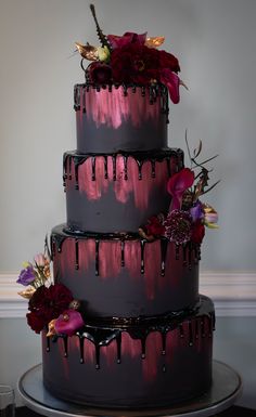 a three tiered cake with flowers and dripping chocolate