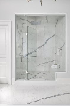 a bathroom with white walls and marble flooring on the shower wall, along with a glass door