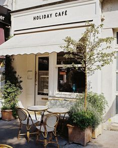 the outside of a restaurant with tables and chairs in front of it, next to potted plants