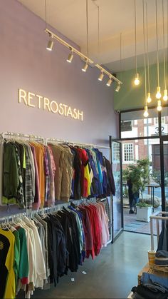 a clothing store with clothes on racks and lights hanging from the ceiling above it's windows