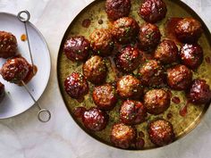 meatballs with sauce and seasoning on a plate next to a platter full of meatballs