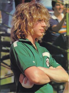 a young man with long hair wearing a green shirt and holding his arms crossed in front of him