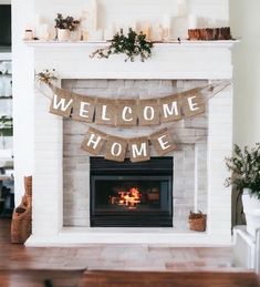 a welcome home banner hanging over a fireplace with candles and potted plants on the mantle