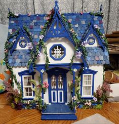 a blue and white doll house with flowers on the roof, sitting on a table